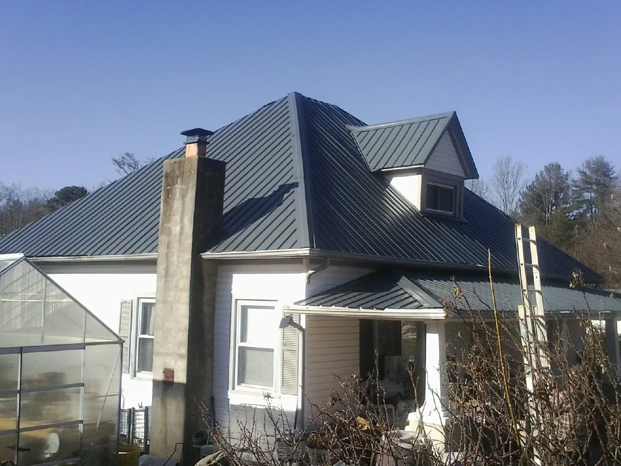 Dark blue standing seam metal roof on a white farmhouse with dormer — Slate & Tile Roof Repair by Roofing Brothers in Elk City