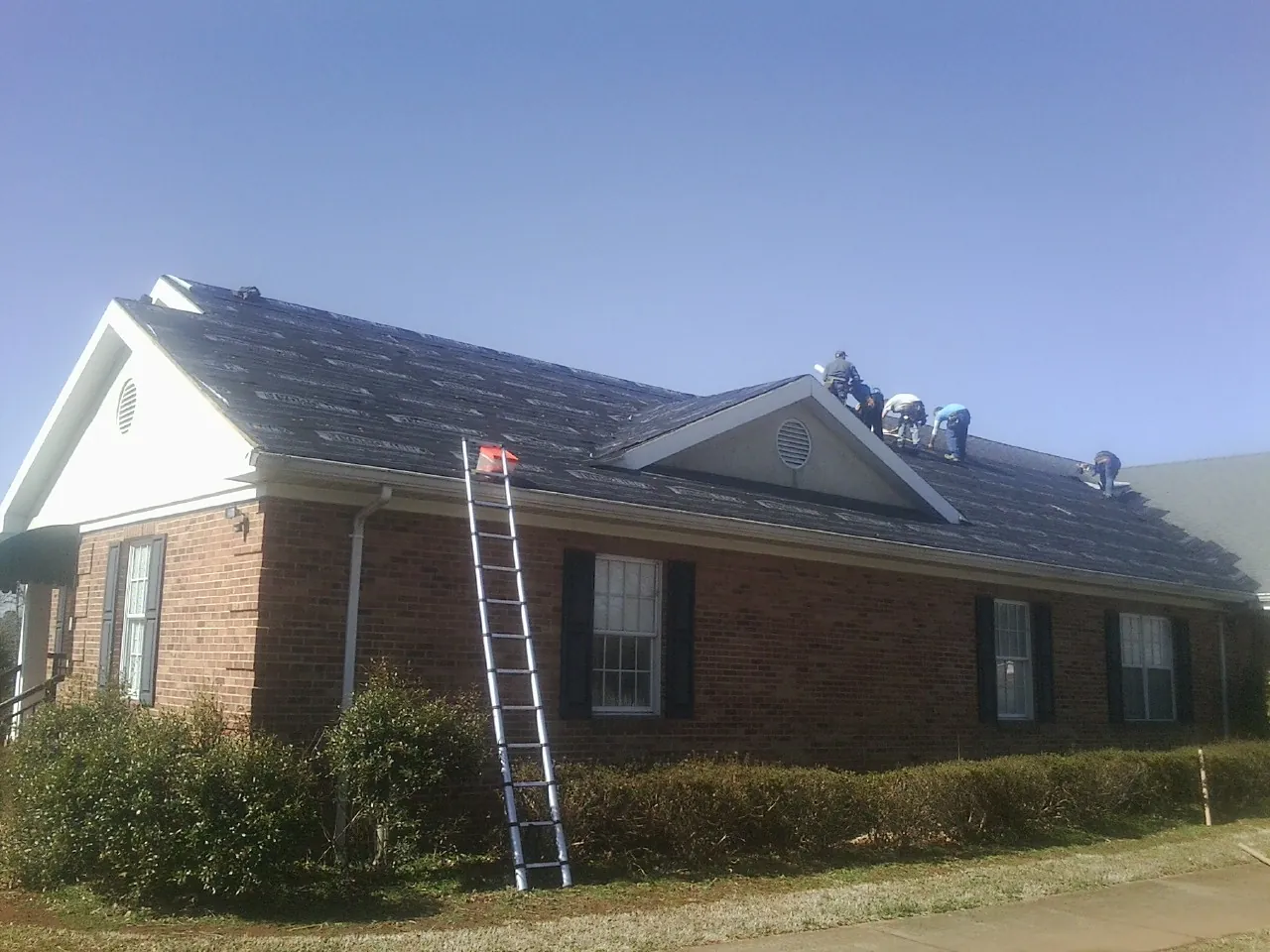 Crew tearing shingles off a brick ranch roof with a ladder set — Metal Roof Repair work by our crew in Elk City