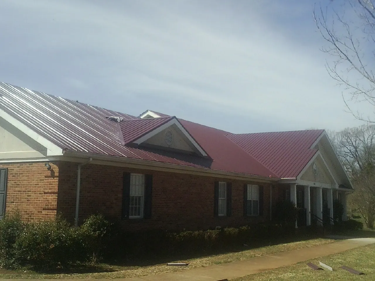 Red metal roof with gabled entries on a long brick building, from a Hail Damage Roof Repair job in Elk City