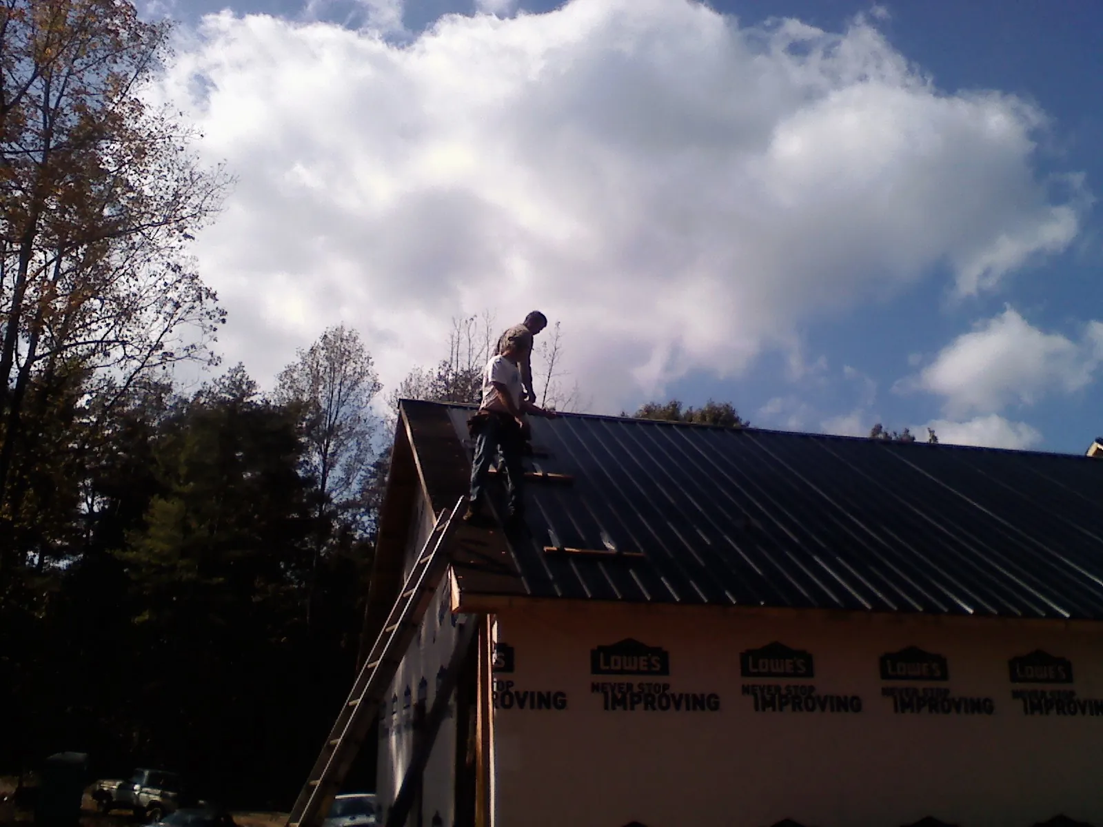 Roofer fastening dark metal panels high against a cloudy sky, from a Roof Inspection job in Elk City