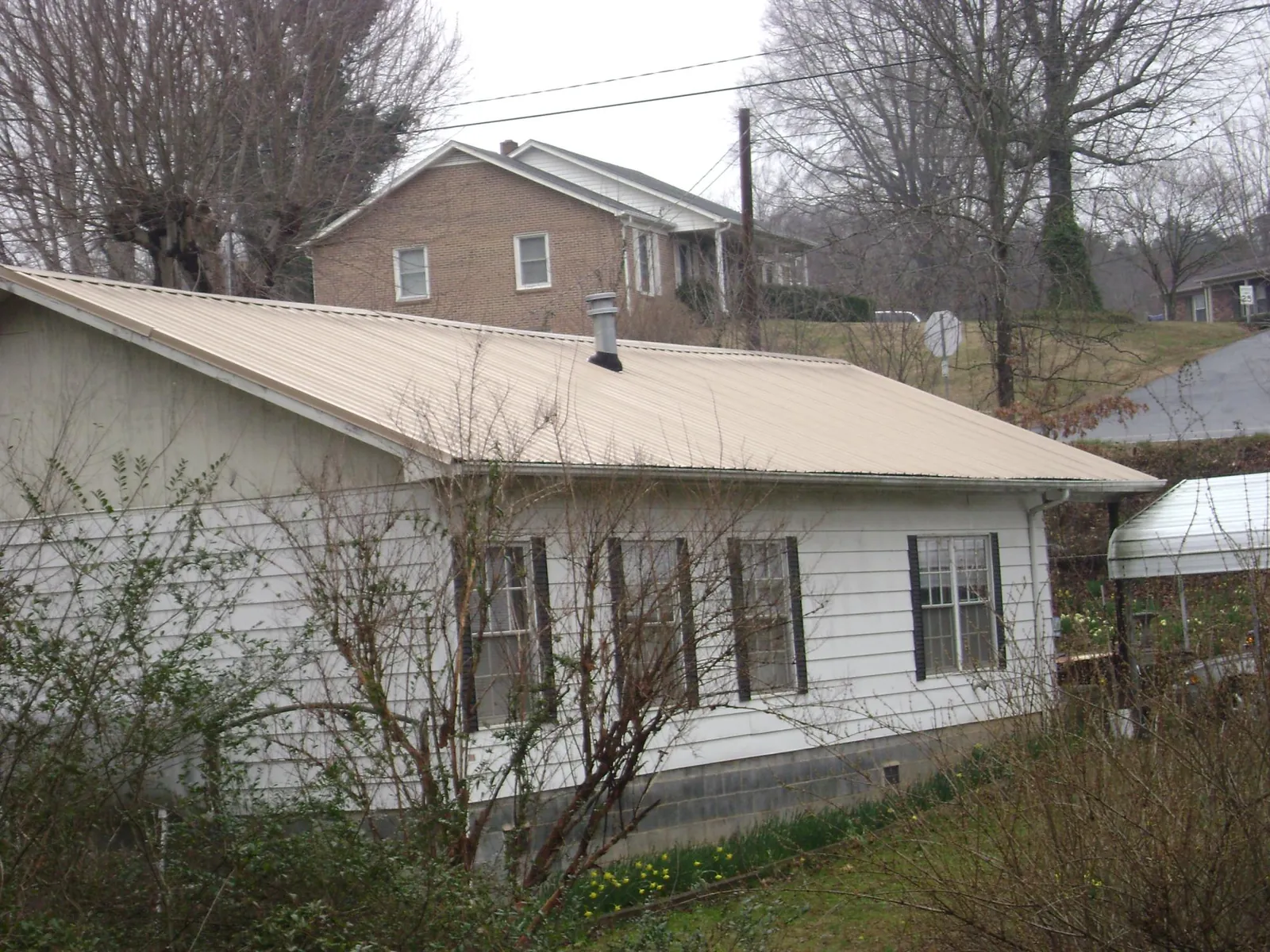 Tan metal roof on a white sided house set into a hillside — Commercial Roofing by Roofing Brothers in Elk City